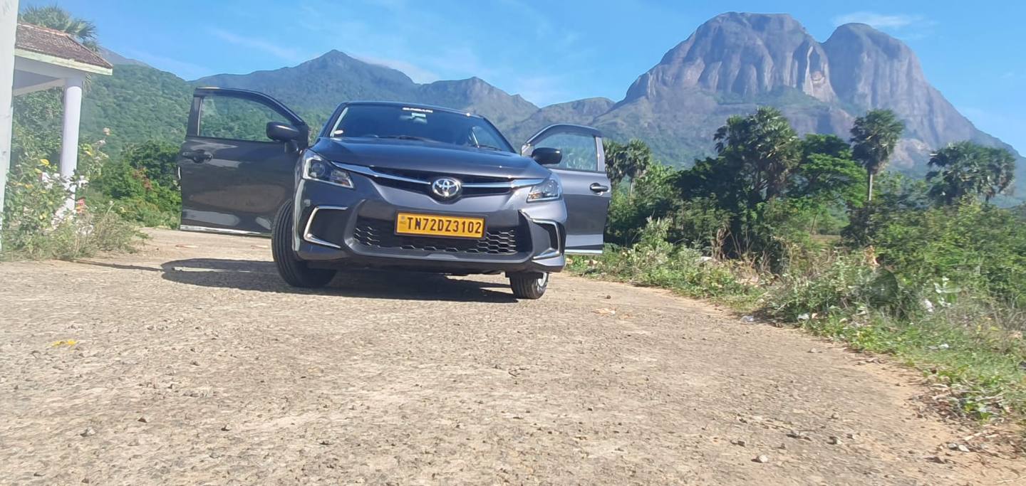 Our grey Toyota Glanza taxi with its doors open, hills behind